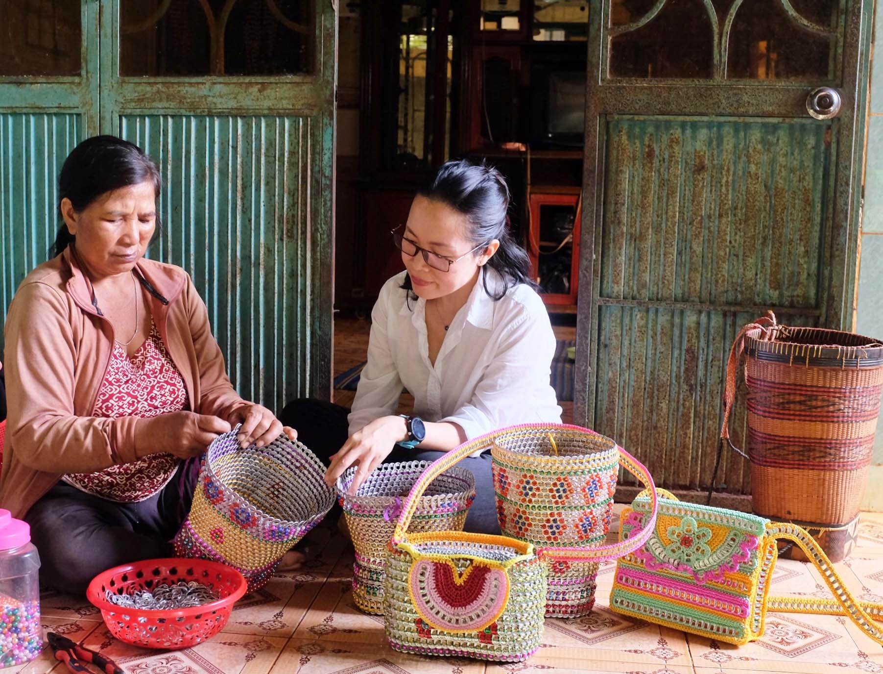 Chị Rơ Mah Vo (bìa trái) giới thiệu các sản phẩm thủ công mỹ nghệ do mình làm với tác giả bài viết. Ảnh: Minh Châu