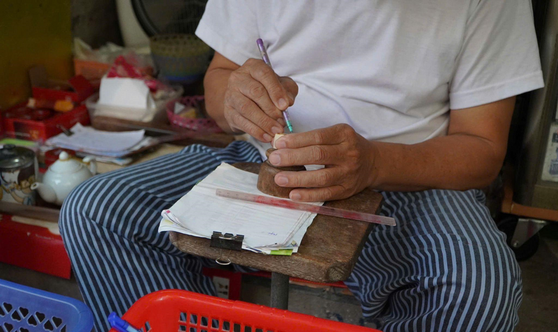 Đôi bàn tay tỉ mỉ của bác Toàn khi phác thảo hình lên mặt con dấu để khắc cho khách. Ảnh: Châu Anh